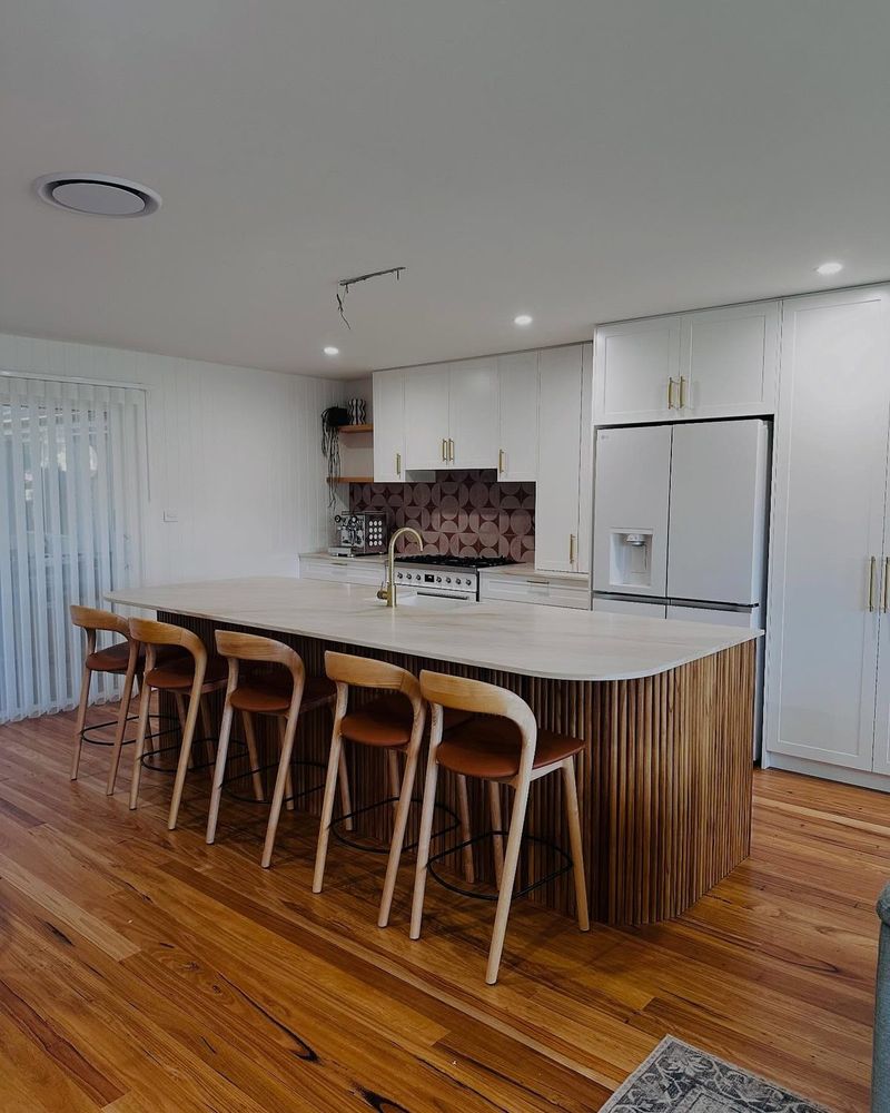 Renovated open-plan kitchen with a long stone-topped island, timber stools and Blackbutt floors, Boambee East