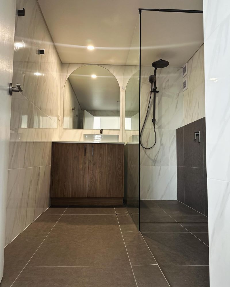 Renovated bathroom with a frameless shower, arched mirror and timber vanity, Coffs Harbour apartment