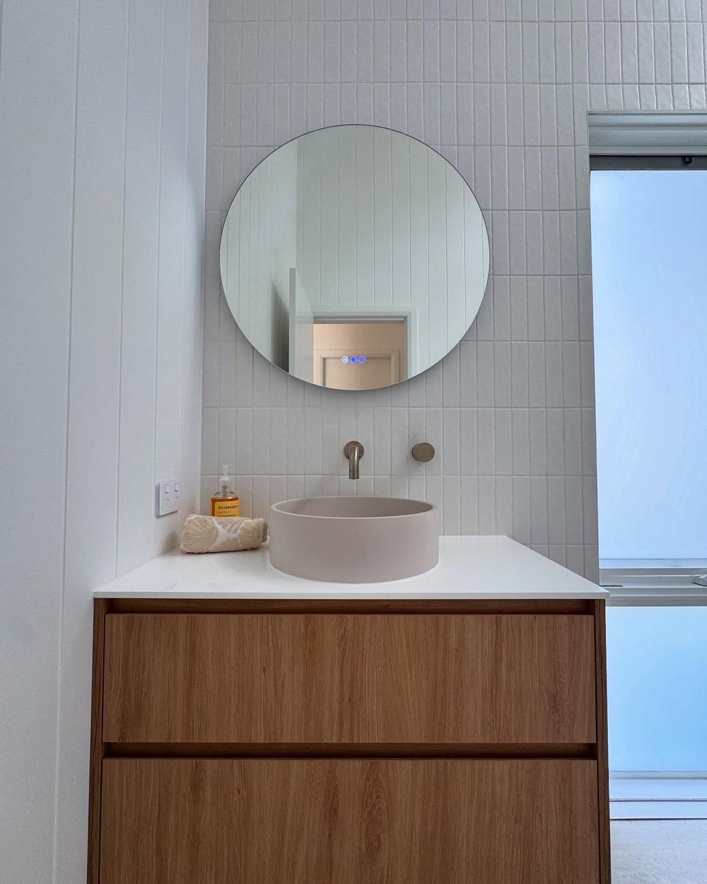 Renovated bathroom with a round mirror, timber vanity, stone basin and white vertical tiles