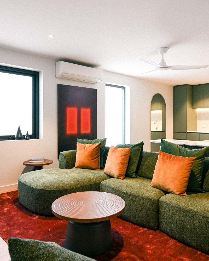 Renovated hotel suite living area with a curved green lounge, orange cushions, a red rug and red artwork, Plantation Hotel