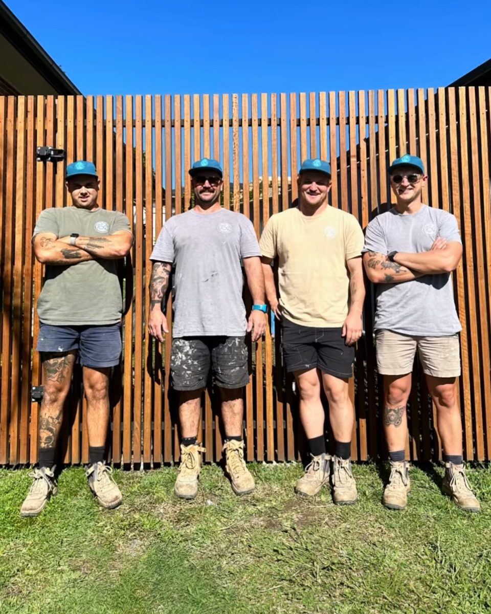 Four T&A Builders crew members in matching caps and shirts, standing in front of Blackbutt timber screening